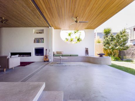 Airy interior with wooden ceiling, large window, and concrete furniture pieces.