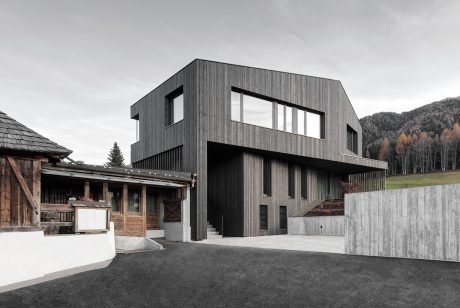 Modern, wood-clad building with large windows, concrete retaining wall, and wooden structure in foreground.