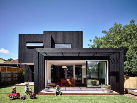 A modern, black-clad home with a large, open-plan living area leading to the backyard.