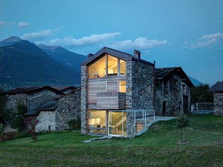 Striking stone and wood structure with illuminated interiors, nestled in scenic mountains.