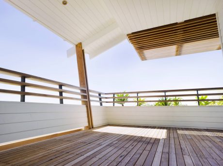 Spacious covered balcony with wooden slat ceiling and railings, overlooking lush greenery.
