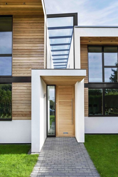 A sleek, modern exterior with a wooden facade, glass-paneled entryway, and landscaped yard.
