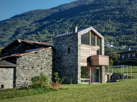 A modern mountain retreat with a stone exterior and large windows overlooking lush foliage.