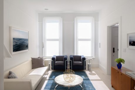 Minimalist living room with large windows, white walls, and a geometric coffee table.