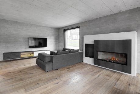 Minimalist living room with concrete walls, wooden flooring, and a modern fireplace.
