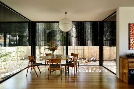 Minimalist dining room with large windows, wooden table and chairs, and hanging sphere light.