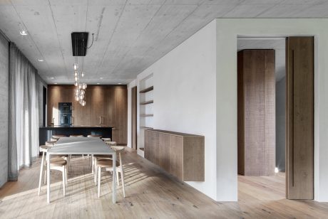 A modern, open-concept dining area with a sleek, minimalist kitchen and wood-paneled walls.