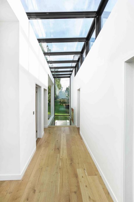 Expansive glass-enclosed hallway with wooden floors leading to an outdoor garden.