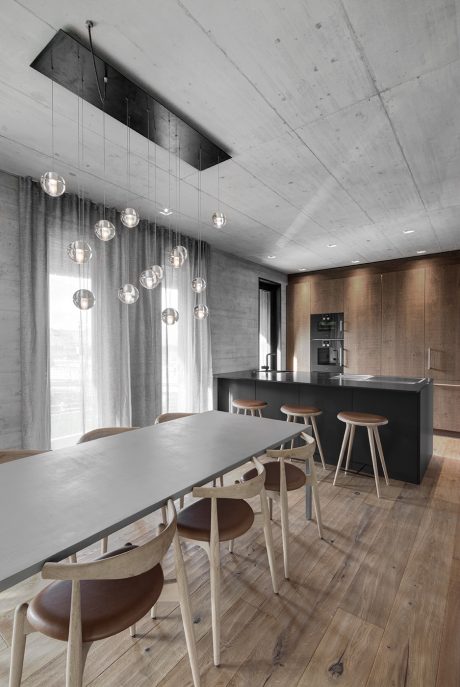 A modern kitchen with a sleek and minimalist design, featuring a black island, wooden floors, and suspended globe lights.