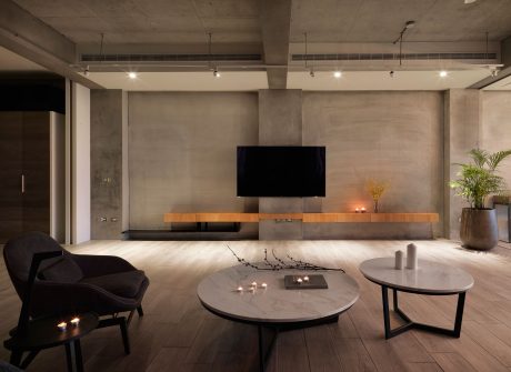 Minimalist living room with concrete walls, wooden TV cabinet, and marble coffee tables.