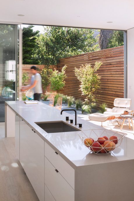 Modern outdoor kitchen with sleek counters, wooden privacy fence, and lush greenery.