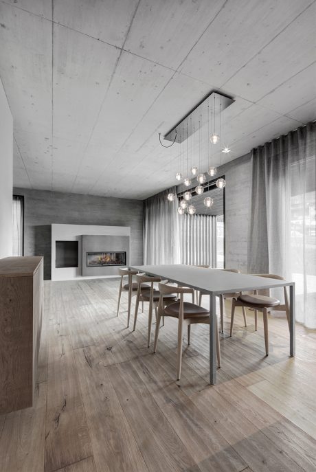 Minimalist dining room with pendant lighting, concrete walls, and wooden floor.