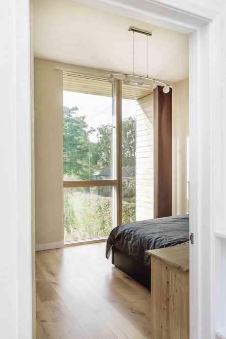 Spacious bedroom with large window, wood furniture, and modern lighting fixtures.