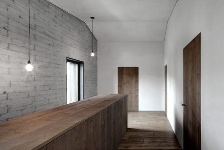 A minimalist, industrial-style interior featuring concrete walls, wooden furniture, and pendant lighting.