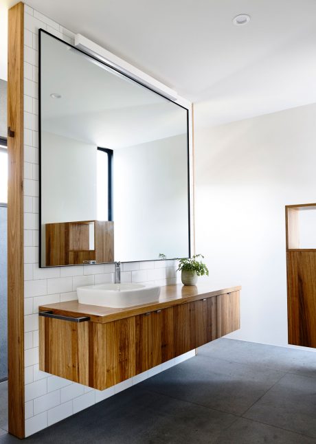 A minimalist bathroom with a floating wooden vanity, large mirror, and white subway tiles.