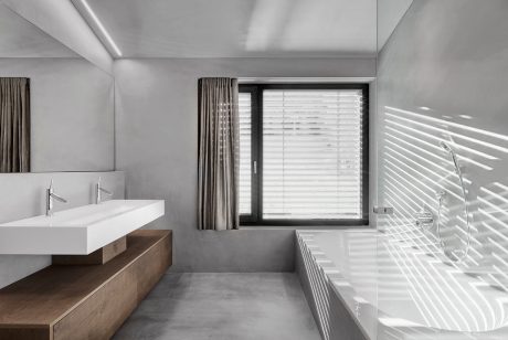 Modern, minimalist bathroom with white vanity, wood accents, and large window with blinds.
