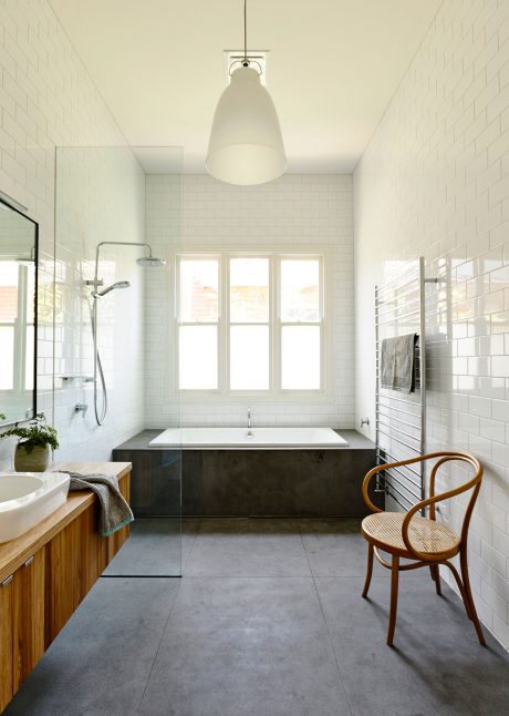 Sleek, modern bathroom with tiled walls, concrete floor, freestanding tub, and vintage chair.