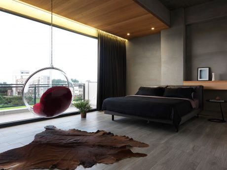 Cozy bedroom with suspended bubble chair, wooden ceiling, and large window offering scenic view.