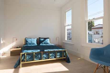 Bright, modern bedroom with large window, minimalist furniture, and vibrant teal bedding.