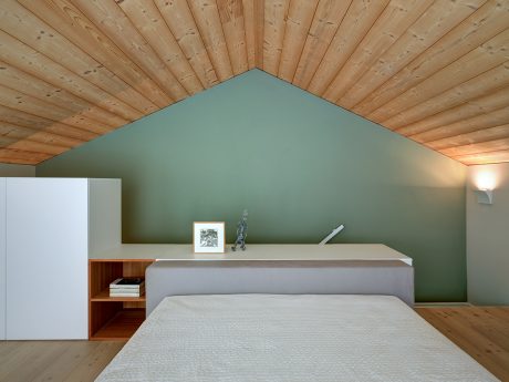 Cozy bedroom with wooden ceiling, green accent wall, and integrated storage.