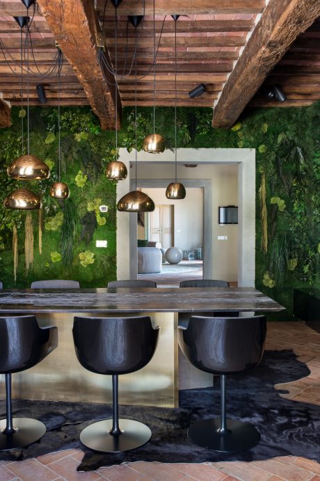A rustic dining room with a lush moss-covered wall, wooden ceiling beams, and pendant lights.