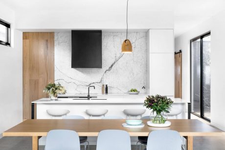 A modern kitchen with a marble backsplash, wooden table, and pendant lighting creating a sleek, minimalist space.