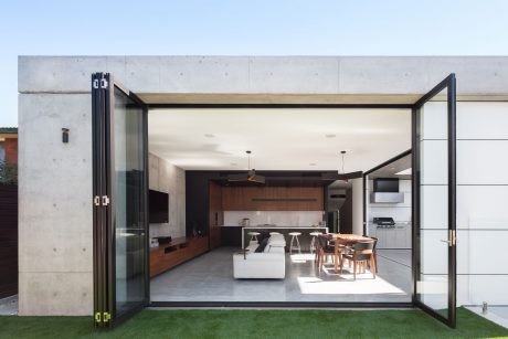 Modern open-plan living space with glass doors, concrete walls, and wooden furniture.