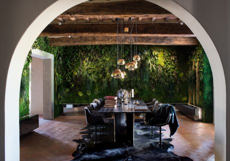 A rustic, nature-inspired dining space with a lush green wall and hanging light fixtures.