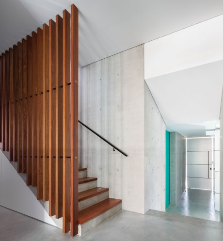 Modern staircase with wooden steps and concrete walls, leading to a hallway.