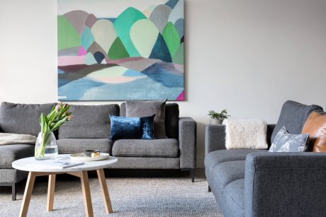 Cozy living room with gray sofas, colorful abstract painting, and wooden coffee table.