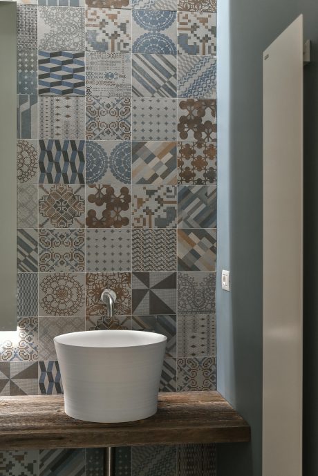 A modern bathroom featuring a patterned tile wall and a white round sink on a wooden counter.