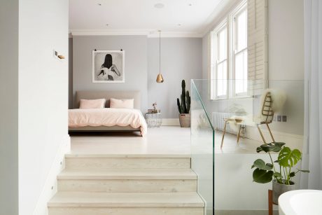 Bright, airy bedroom with wooden steps, large windows, and a modern glass partition dividing the space.