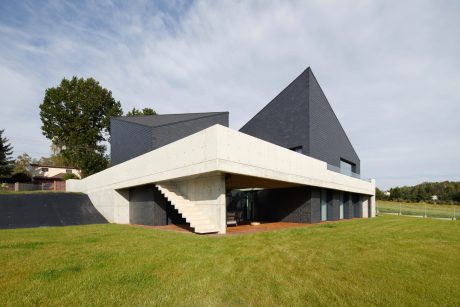 Modern architectural structure with distinct angular roofs and concrete facade against green lawn.