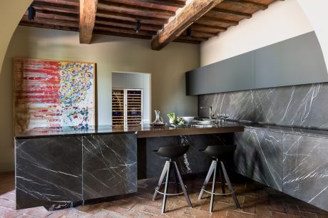 A modern kitchen with sleek black marble countertops, wooden beams, and a vibrant abstract artwork.