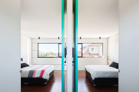 The image showcases a modern, minimalist bedroom with clean lines, large windows, and contrasting turquoise accents.