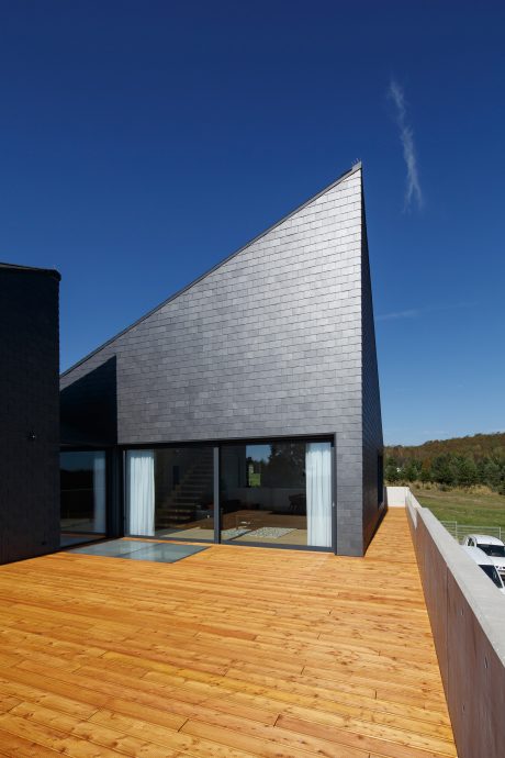 A modern, angular building with a large wooden deck and expansive glass windows overlooking nature.