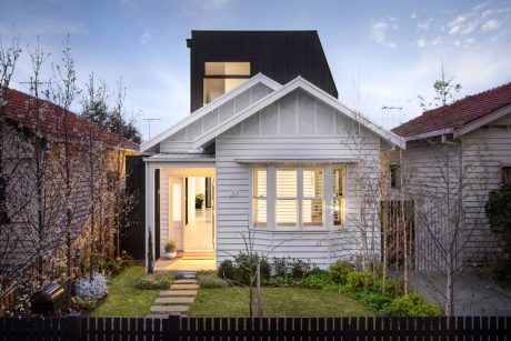 Gray wooden cottage-style home with sloped roof, large windows, and cozy front porch.