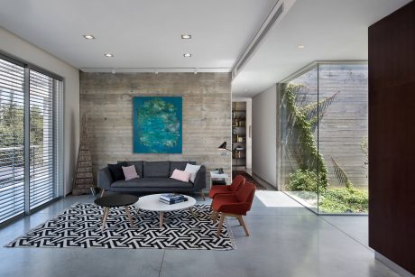A modern living room with concrete walls, a large black sofa, and a vibrant blue abstract painting.
