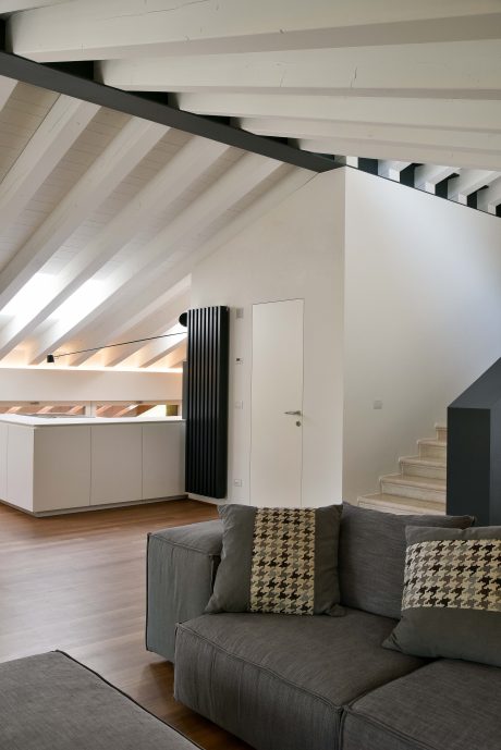 Modern open-plan living space with exposed wooden beams, sleek gray sofa, and minimalist decor.