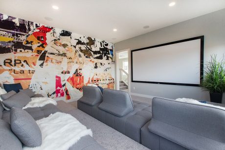 Sleek modern home theater with abstract mural wall, plush gray seating, and large projection screen.