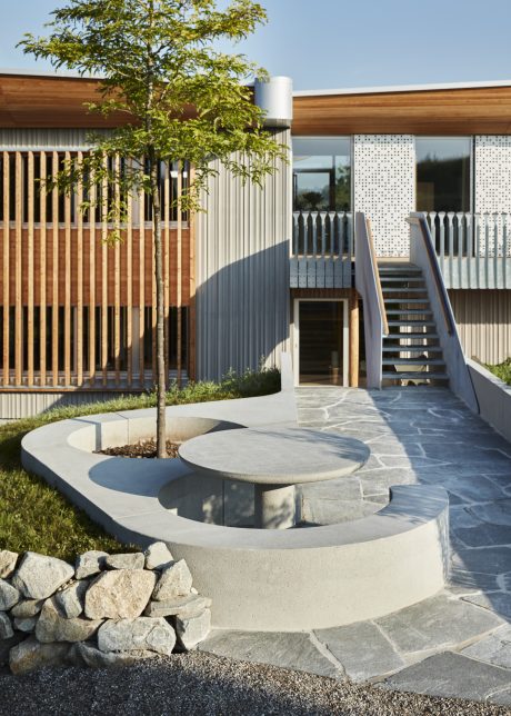Wooden facade, patterned screens, stone steps and seating on a landscaped exterior.