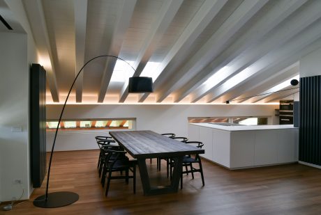 Striking vaulted ceiling with wood beams, minimalist kitchen, and dining table with black chairs.