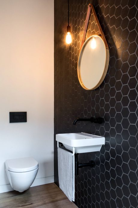 A modern bathroom with a round mirror, hexagonal dark tiles, and a white sink vanity.