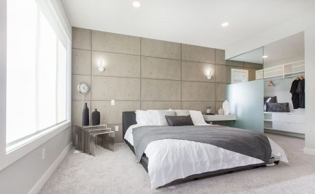 Minimalist bedroom with concrete-paneled walls, recessed lighting, and neutral color scheme.