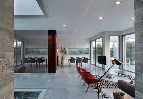 Spacious modern interior with concrete walls, large windows, and a mix of black and red furniture.