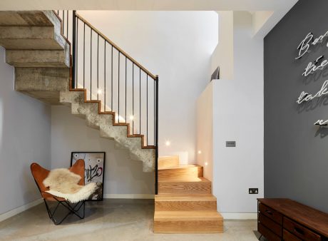 Wooden stairs with metal railings lead to upper level; leather chair and chalkboard wall add industrial charm.