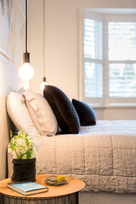 Cozy bedroom interior with hanging pendant lights, plush bedding, and a decorative vase.