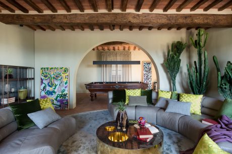 A cozy and eclectic living room with exposed wooden beams, archways, and vibrant decor.