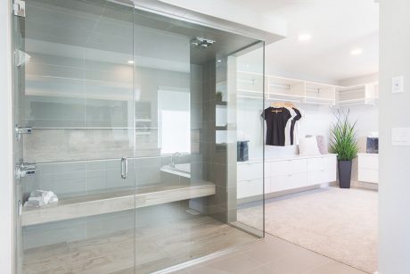 Elegant bathroom with glass shower enclosure and open closet area with clothing.