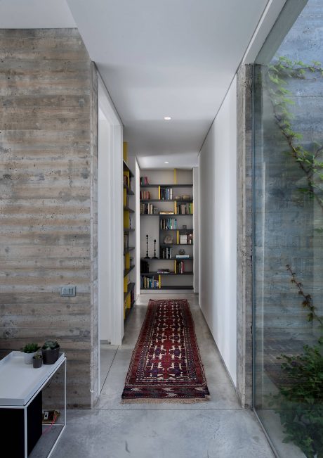 A modern hallway with concrete walls, built-in shelving, and a vibrant patterned rug.